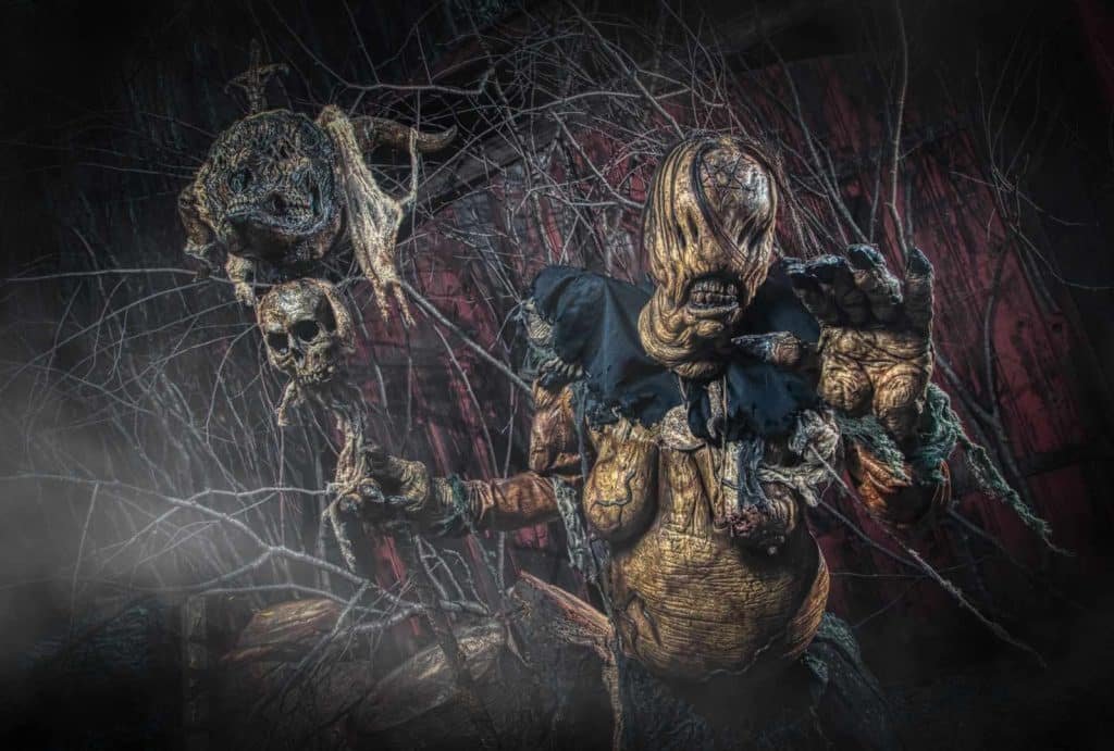 Scarecrow character with a grotesque appearance, holding a staff adorned with a skull and a frog, surrounded by dark foliage, showcasing a fantasy-themed photography style by Nimble Dragon Studios.