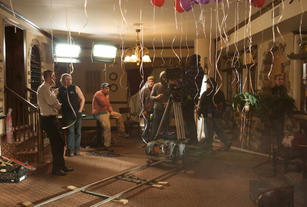 Film crew setting up equipment in a decorated indoor space with balloons, showcasing a behind-the-scenes moment of a photography or video shoot.