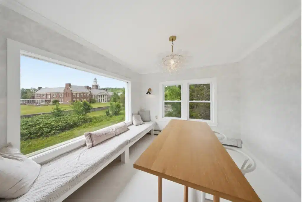 Bright studio workspace with wooden desk overlooking manicured campus grounds and historic brick building.