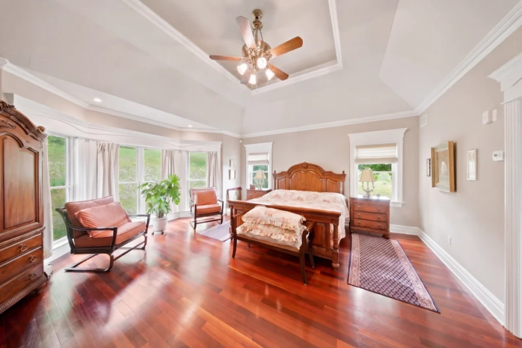 Spacious master bedroom with wooden furniture, hardwood floors, and abundant natural light from bay windows.