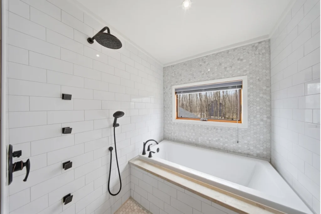Modern bathroom with white subway tile, rainfall showerhead, soaking tub, and woodland window view.
