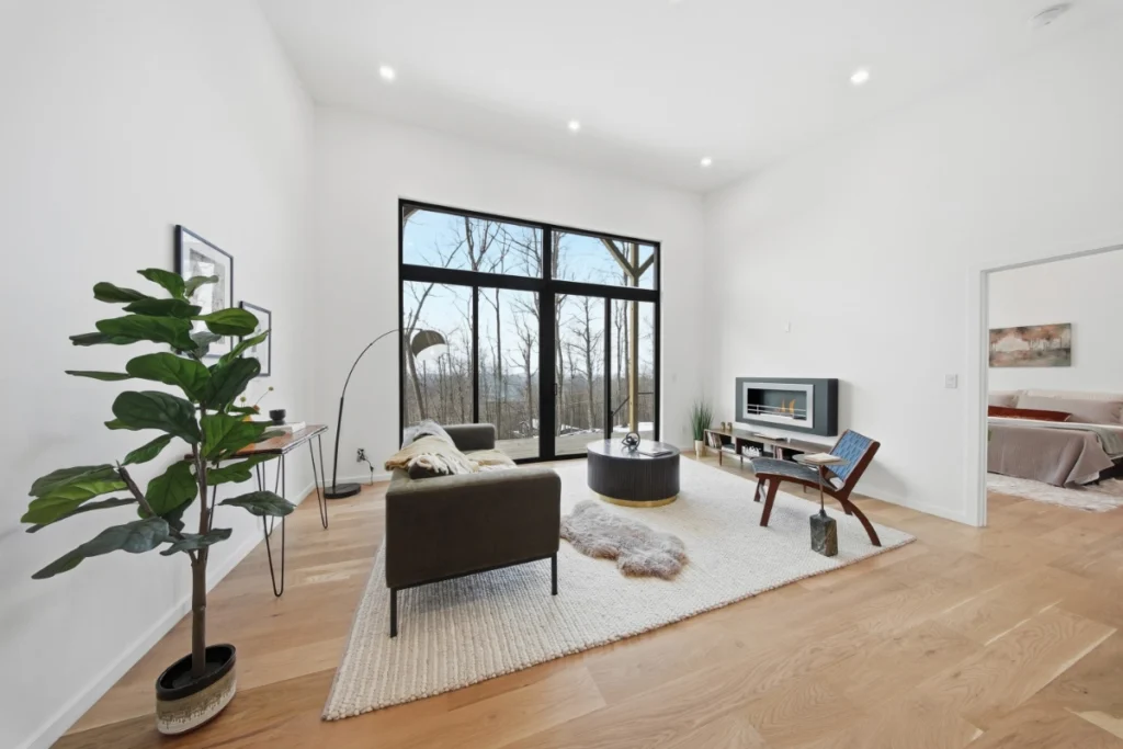 Modern living room with large windows, wooden floors, and minimalist furnishings.
