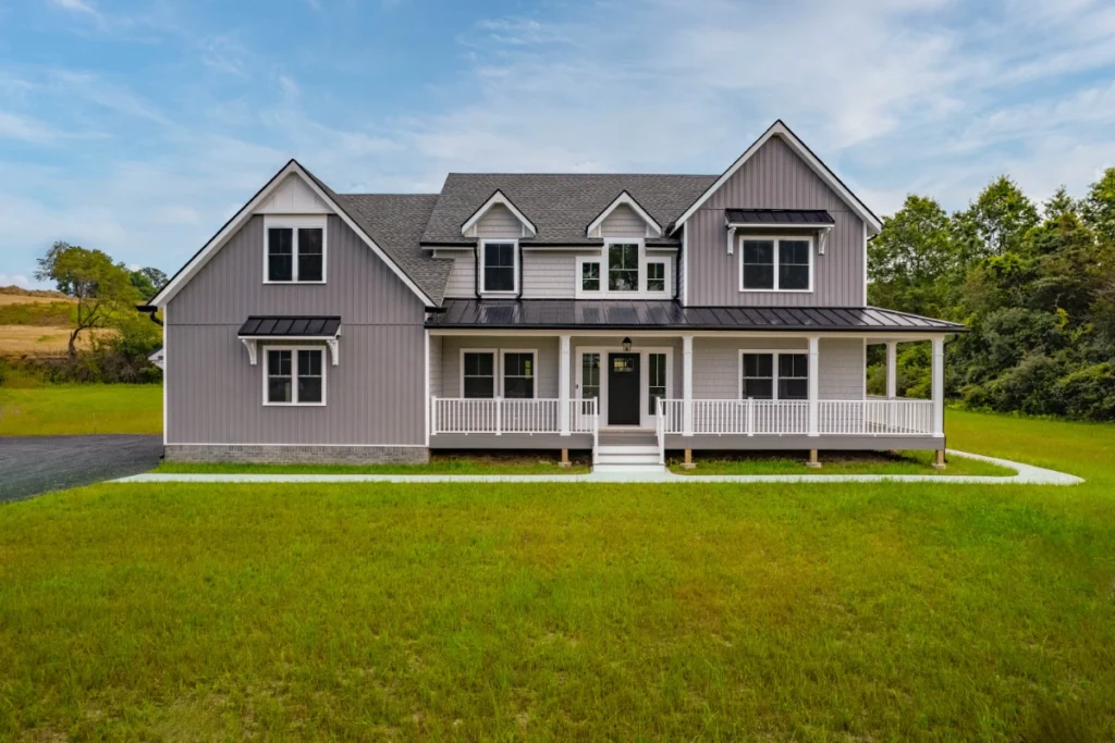 Modern farmhouse with gray siding and white porch on expansive green lawn.