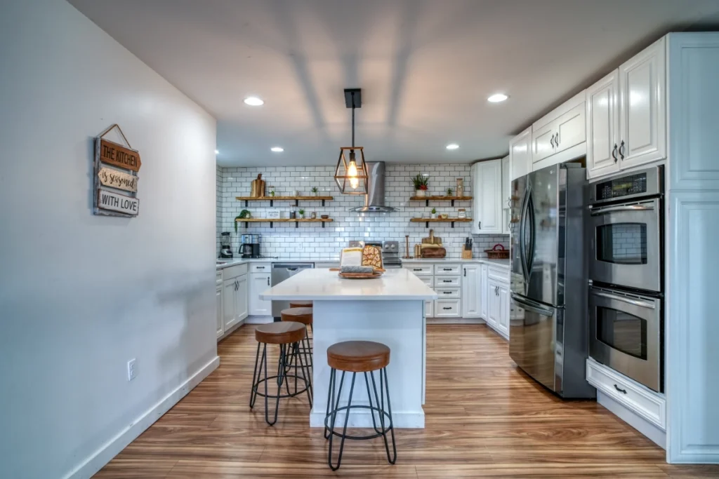 Modern white kitchen with island seating, wooden floors, and stainless steel appliances.